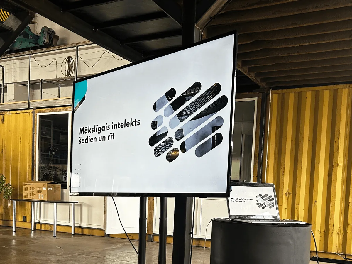 Экран и ноутбук, подготовленные к лекции BalticAI, с названием на латышском языке «Искусственный интеллект сегодня и завтра»